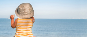 Un bebe en la playa se protege del sol con un gorrito